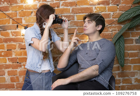 Girl photographer photographs a guy against a brick wall Girl photographer photographs a guy against a brick wall 109276758