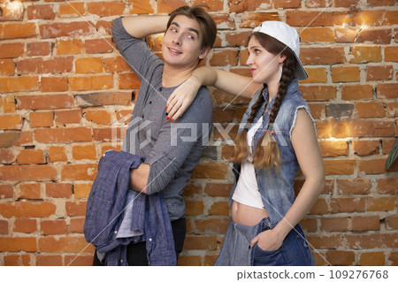 A guy and a girl are standing against a brick wall. Young couple in jeans clothes 109276768