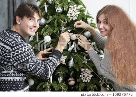 A man and a woman decorate a Christmas tree. Husband and wife at christmas. Preparing for the winter holidays A man and a woman decorate a Christmas tree. Husband and wife at christmas. Preparing for the winter holidays 109276773