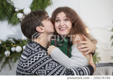 A man gives a woman a Christmas present. Husband and wife in the New Year holidays. Get a surprise in the winter holidays. Christmas holidays concept. A man gives a woman a Christmas present. Husband and wife in the New Year holidays. Get a surprise in the winter holidays. Christmas holidays concept. 109276780