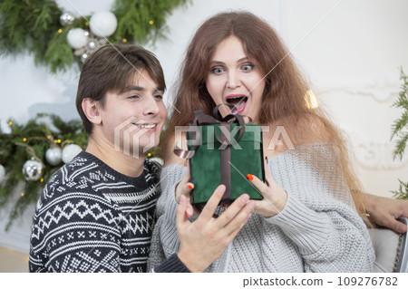 A man gives a woman a Christmas present. Husband and wife in the New Year holidays. Get a surprise in the winter holidays. Christmas holidays concept. A man gives a woman a Christmas present. Husband and wife in the New Year holidays. Get a surprise in the winter holidays. Christmas holidays concept. 109276782