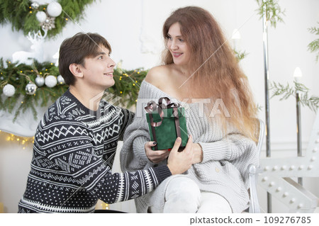 A man gives a woman a Christmas present. Husband and wife in the New Year holidays. Get a surprise in the winter holidays. Christmas holidays concept. A man gives a woman a Christmas present. Husband and wife in the New Year holidays. Get a surprise in the winter holidays. Christmas holidays concept. 109276785