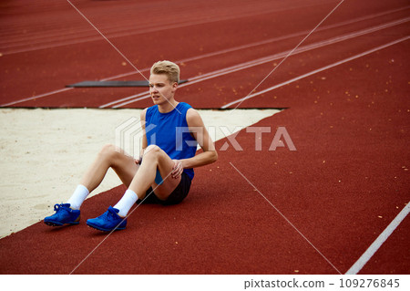 Full length portrait of man sitting on court and warming-up before championship. anticipation of athlete sportsman before crucial leap. Full length portrait of man sitting on court and warming-up before championship. anticipation of athlete sportsman before crucial leap. 109276845