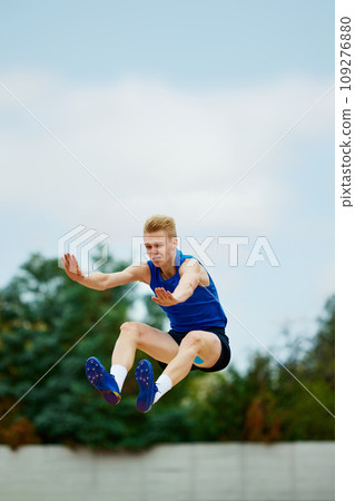 photo capturing climax of long jump, frozen in motion. Athletic man, professional sportsman sets new long jump record. photo capturing climax of long jump, frozen in motion. Athletic man, professional sportsman sets new long jump record. 109276880