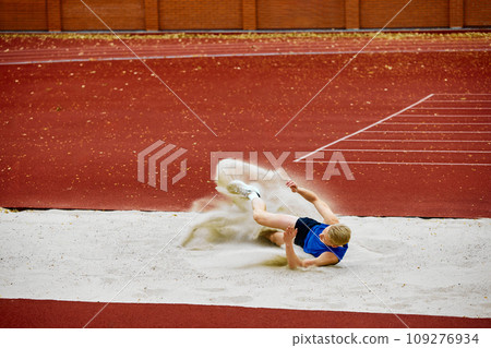 Sandpit landing after an impressive jump. Portrait of motivated young man, professional sportsman doing perfect long jump on championship. Sandpit landing after an impressive jump. Portrait of motivated young man, professional sportsman doing perfect long jump on championship. 109276934