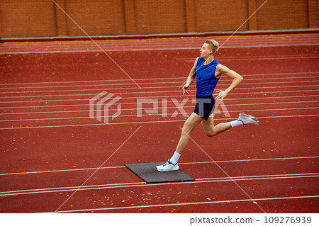 Strategically timed leap for optimal distance. Young attractive sportsman running on sport court to make a perfect long jump to sand. 109276939