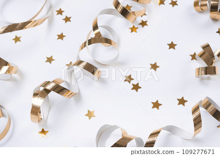 flat composition of golden ribbons or serpentine and golden confetti in the form of stars on a white background. The concept of a birthday, anniversary or holiday in golden colors. flat composition of golden ribbons or serpentine and golden confetti in the form of stars on a white background. The concept of a birthday, anniversary or holiday in golden colors. 109277671