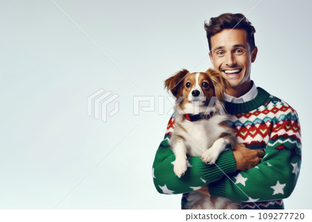 Banner, poster with copy space for International Ugly Sweater Day. White man in colorful, hilariously terrible sweater, cheerfully laughing, holding adorable purebred toy spaniel puppy dog. Mock up 109277720