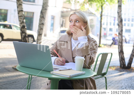 Image of woman sitting with laptop outside on street, using laptop, looking surprised, amazed by something she saw online Image of woman sitting with laptop outside on street, using laptop, looking surprised, amazed by something she saw online 109278085