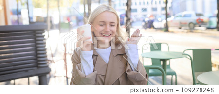 Portrait of cheerful young blond woman, enjoying spending time in outdoor cafe, drinking coffee and laughing, having casual meet up in street restaurant 109278248