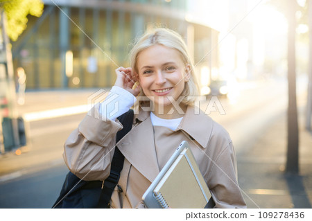 Young blonde woman, college student on street, holding journals and notebook, carry her homework material, going to university, smiling and looking happy 109278436