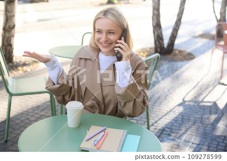Close up portrait of happy, charismatic young woman talking on mobile phone, sitting in cafe alone, outside on sunny day, answer a call, having friendly conversation Close up portrait of happy, charismatic young woman talking on mobile phone, sitting in cafe alone, outside on sunny day, answer a call, having friendly conversation 109278599