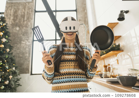 Using a virtual reality headset, a young and beautiful woman prepares food in the kitchen. Using a virtual reality headset, a young and beautiful woman prepares food in the kitchen. 109278608