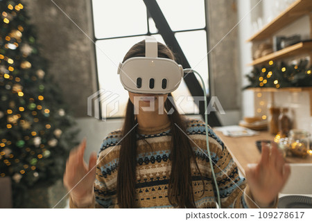 Utilizing a virtual reality headset, a beautiful and stylish girl prepares a Christmas recipe in the kitchen. 109278617