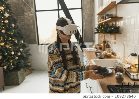 Engaged in holiday cooking, a beautiful and stylish girl uses a virtual reality headset for the recipe in the Christmas kitchen. 109278640