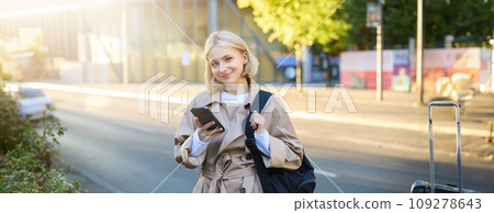 Smiling, beautiful young woman with backpack, holding smartphone, standing on street, using mobile phone app Smiling, beautiful young woman with backpack, holding smartphone, standing on street, using mobile phone app 109278643