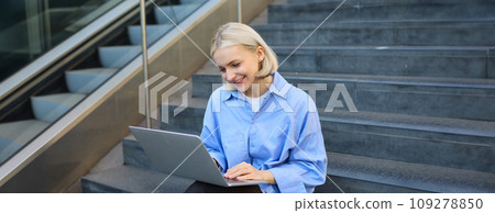 Smiling girl student using laptop computer modern technology device outdoor in university campus online learning, elearning outside sitting on urban stairs. Web education course webinars concept Smiling girl student using laptop computer modern technology device outdoor in university campus online learning, elearning outside sitting on urban stairs. Web education course webinars concept 109278850