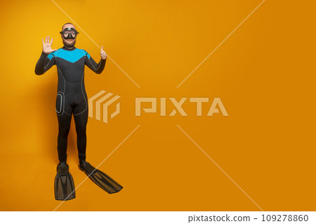 Scuba diver man showing six fingers up on yellow studio wall background Scuba diver man showing six fingers up on yellow studio wall background 109278860