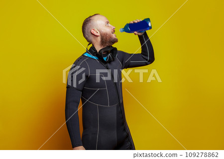Scuba diver man drinking on yellow studio wall background Scuba diver man drinking on yellow studio wall background 109278862