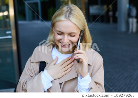 Close up portrait of smiling, laughing young woman, talking on mobile phone, standing outdoors, walking on street with smartphone and chatting 109279263