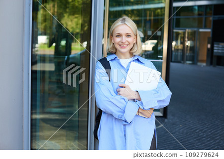 Image of young college girl, young woman with laptop, posing near university building, standing on street, smiling, concept of education and people 109279624
