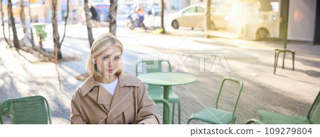 Vertical shot of young blond woman in wireless headphones, making notes, studying online, attend web lecture, using laptop, writing in notebook, looking serious at camera Vertical shot of young blond woman in wireless headphones, making notes, studying online, attend web lecture, using laptop, writing in notebook, looking serious at camera 109279804