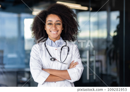 Portrait of beautiful female doctor inside office of modern clinic, female doctor smiling and looking at camera with crossed arms, female worker with stethoscope and white medical coat at workplace. 109281953