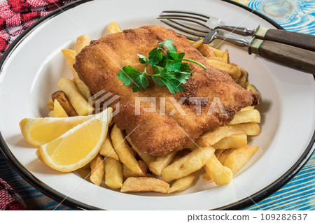A piece of fried cod with fries on a plate. A piece of fried cod with fries on a plate. 109282637