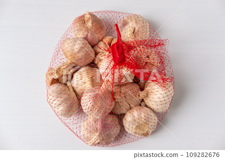 A large head of garlic is in a red mesh package on a white background. A large head of garlic is in a red mesh package on a white background. 109282676