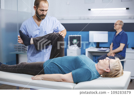 Chiropractor trying to relieve pressure from knee of old patient with arthritis and injury. Physiotherapist cracking leg bones for relief and physical recovery of senior woman with pain. 109283879
