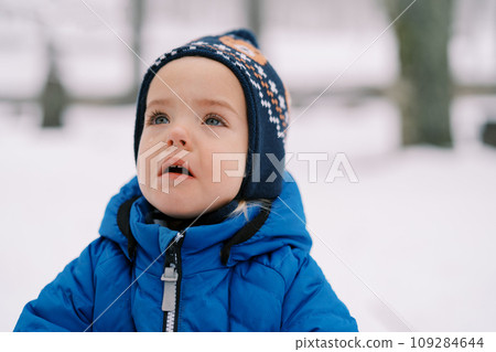Little crying girl with tears in her eyes stands in the snow and looks up 109284644