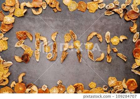 Word made of pieces of dried fruits on a dark cement background in a fruit frame. Caption: Snack 109284707
