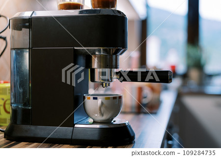 Coffee dripping from the portafilter of a carob coffee machine into a cup on a stand Coffee dripping from the portafilter of a carob coffee machine into a cup on a stand 109284735