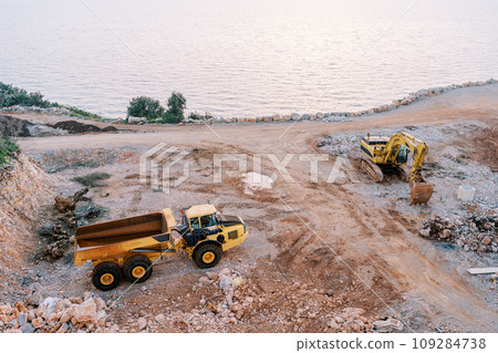 Truck stands next to an excavator in a quarry on the seashore. Top view Truck stands next to an excavator in a quarry on the seashore. Top view 109284738