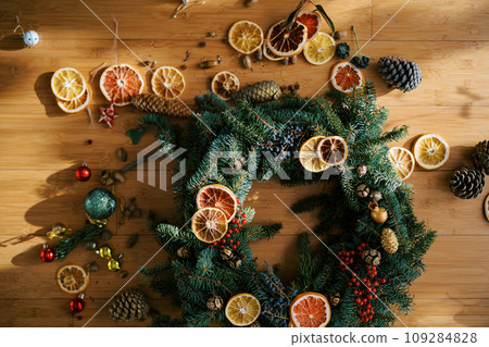 Pieces of dried oranges, toys and fir cones lie near the Christmas wreath on the floor Pieces of dried oranges, toys and fir cones lie near the Christmas wreath on the floor 109284828