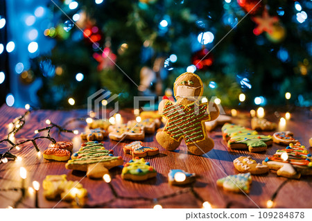 Cookie-man in a mask stands on the table among spread glazed cookies and shining garlands Cookie-man in a mask stands on the table among spread glazed cookies and shining garlands 109284878