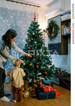 Little girl watches her mother decorate the Christmas tree. Back view 109284896