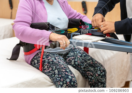 A care staff using a power assist to lifts a patient at nursing home. 109286903