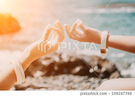Close up Yoga Hand Gesture of Woman Doing an Outdoor meditation. Blurred sea background. Woman on yoga mat in beach meditation, mental health training or mind wellness by ocean, sea Close up Yoga Hand Gesture of Woman Doing an Outdoor meditation. Blurred sea background. Woman on yoga mat in beach meditation, mental health training or mind wellness by ocean, sea 109287398