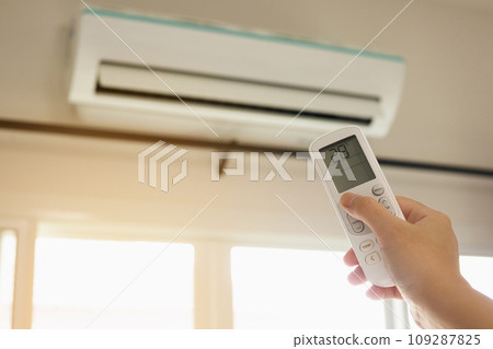 Hand with remote control directed on air conditioner inside the room 109287825