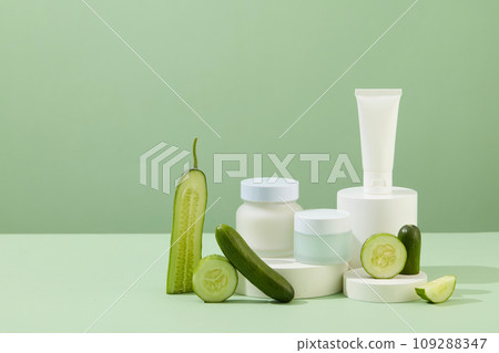 Cosmetic bottles without labels for branding are placed on a white podium. Fresh cucumbers are placed on the side. Skin care with products from cucumber extract. 109288347