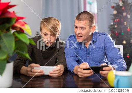 Happy father and son together playing on their smartphones while sitting at the table at home during celebration of christmas 109288909