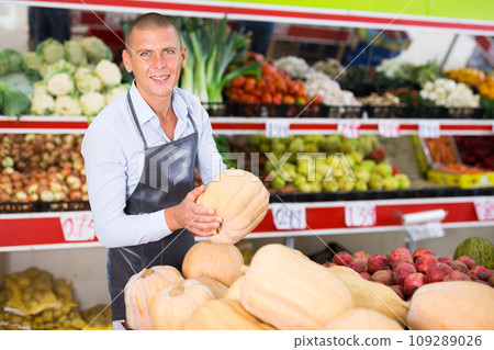 Smiling greengrocery owner laying out fruits and vegetables on counter Smiling greengrocery owner laying out fruits and vegetables on counter 109289026