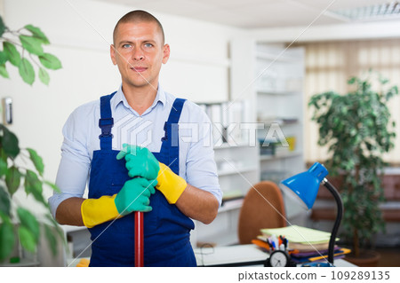 Positive man in overalls cleaning office floor by cleanser 109289135