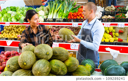 Supermarket worker helping woman to choose melon Supermarket worker helping woman to choose melon 109289241