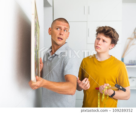 Son and dad hanging picture of lilac on wall Son and dad hanging picture of lilac on wall 109289352