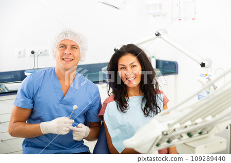 Portrait of a smiling man dentist with a positive woman patient sitting in a dental chair 109289440