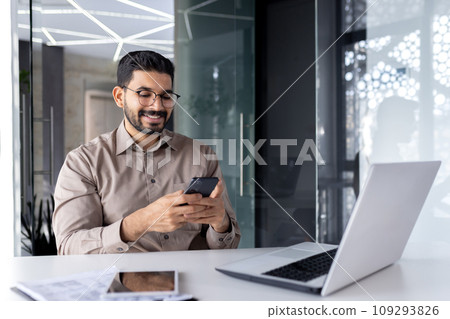 Businessman holding phone inside office, joyful man smiling uses smartphone app at workplace, browses social networks, and writes text message. 109293826