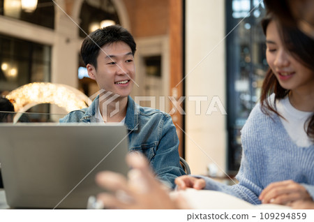 A cheerful young Asian man is listening to his friend's ideas while sitting at a cafe together. 109294859