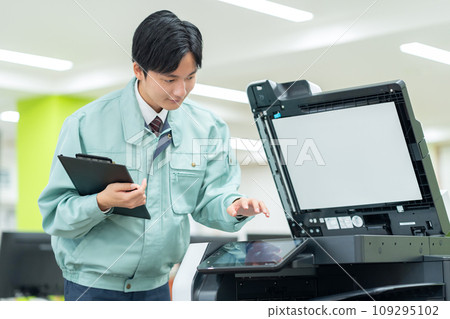 A young male worker maintaining a copy machine in an office A young male worker maintaining a copy machine in an office 109295102